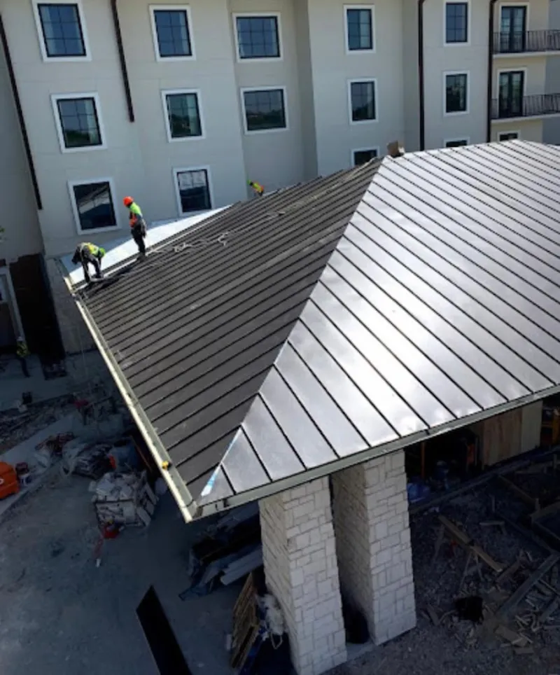 Crew installing standing seam metal roof panels on a commercial project in Lawrence